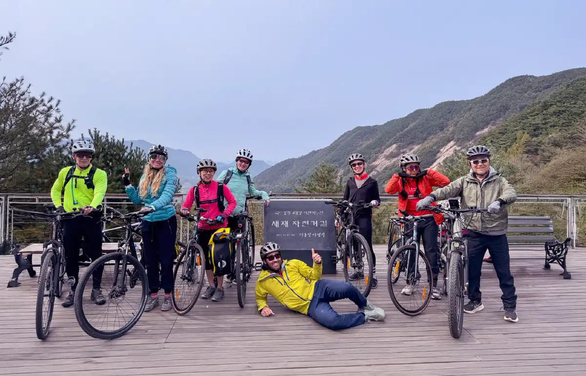 nternational cyclists posing in front of a viewpoint sign on the Saejae Bicycle Path during the Seoul to Andong ride