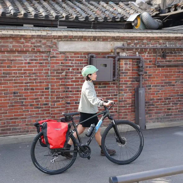 Traveler walking a touring bicycle with pannier bags along a traditional brick wall street in Seoul, South Korea.